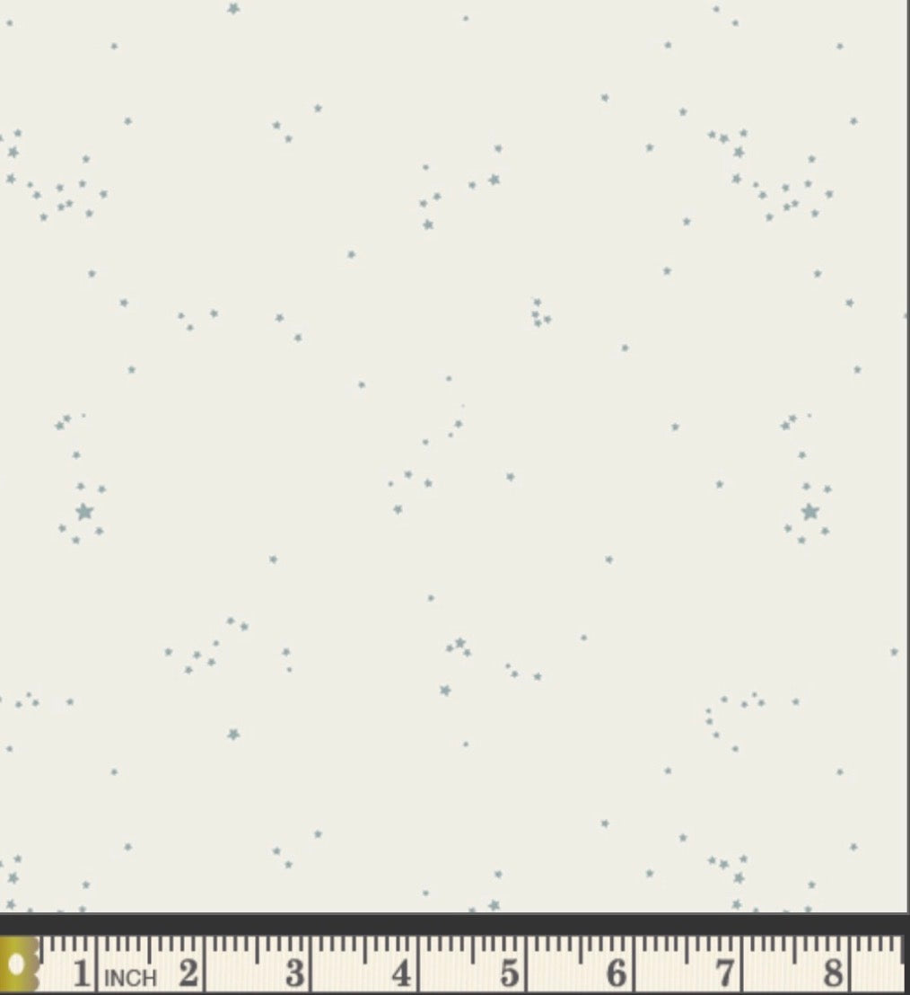 White fabric with small blue star  patterns and a ruler at the bottom for scale.