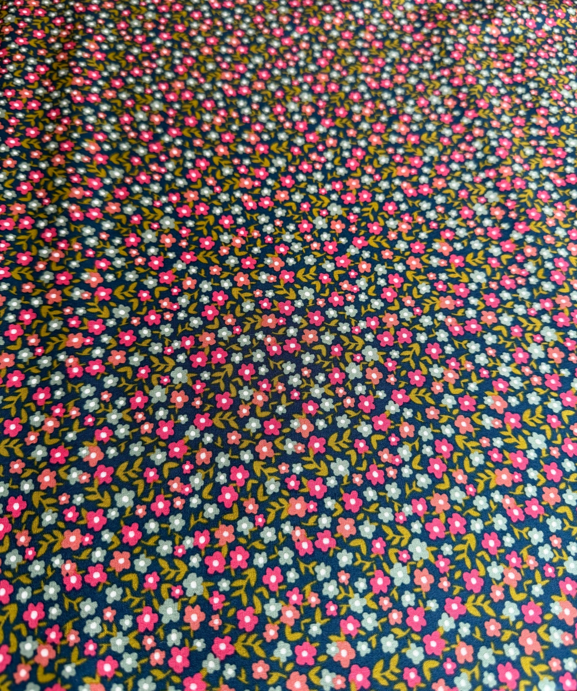 Floral patterned fabric with small pink flowers on a dark blue background