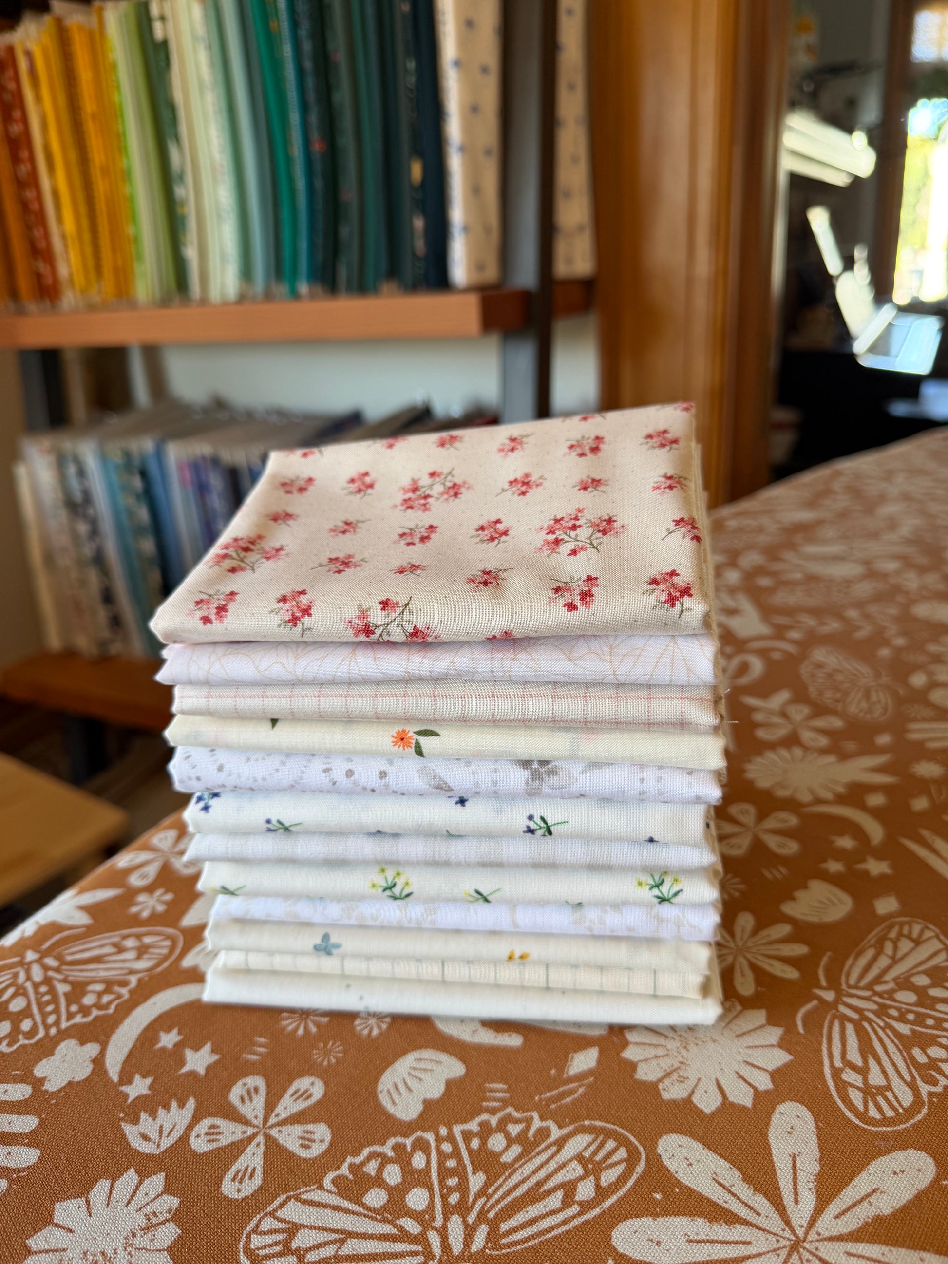 Stack of low volume fabric bundles with floral patterns on a table with a bookshelf in the background